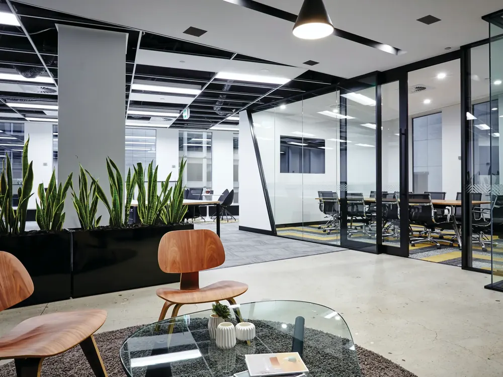 Modern office with glass-walled meeting rooms, a display on the wall and a lounge area in the foreground